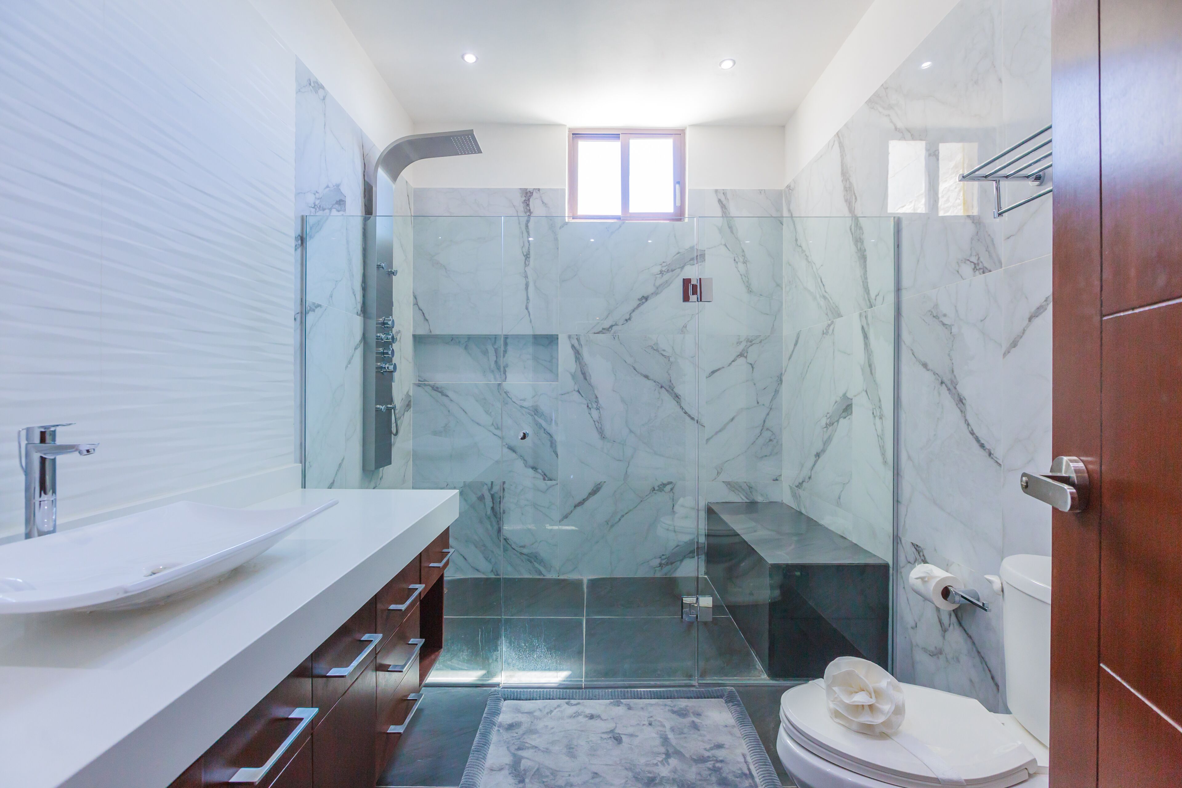A modern bathroom with a glass-enclosed shower, a white sink, and a marble-tiled shower area.