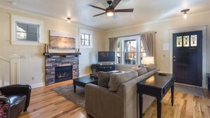 A living room with a fireplace, a sofa, a television, and a ceiling fan. - Bluebird Day - Harmon Park Bungalow, Charming 2BR perfect for getaways! (Bend)