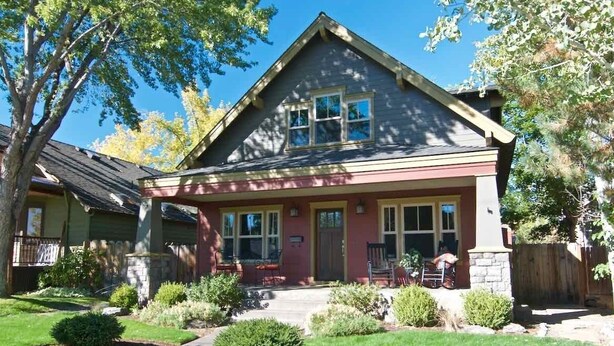 A two-story house with a red and gray exterior, a front porch, and a well-maintained garden. - Bluebird Day - Harmon Park Bungalow, Charming 2BR perfect for getaways! (Bend)