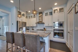 A modern kitchen with white cabinetry, stainless steel appliances, and a bar area with stools. - 6-Seater Golf Cart & 6 Bikes! Spacious Porches! Balconies w/ Views of the Pond! Latitude Adjustment (Santa Rosa Beach)