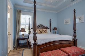 A four-poster bed with a wooden headboard, a bedside table with a lamp, and a red upholstered bench.