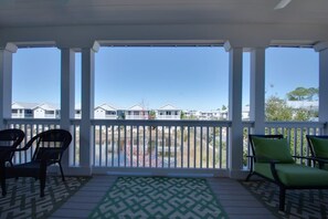 A covered outdoor area with a view of houses in the background, two chairs, and a patterned rug. - 6-Seater Golf Cart & 6 Bikes! Spacious Porches! Balconies w/ Views of the Pond! Latitude Adjustment (Santa Rosa Beach)