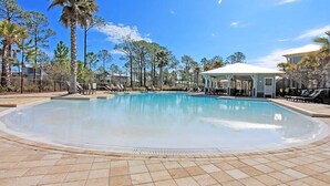 Una grande piscina esterna con bordo piastrellato, circondata da palme e un gazebo.