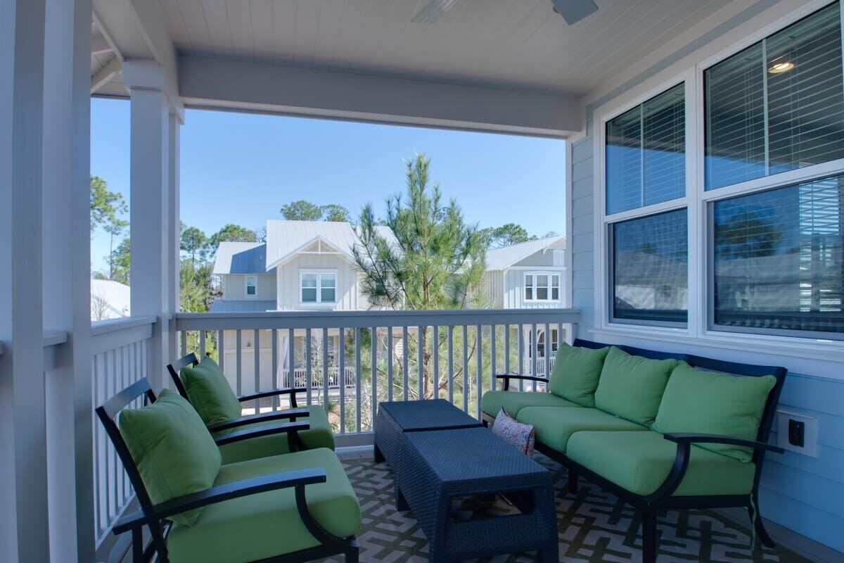 A covered porch with a seating area, including a sofa and chairs, and a view of neighboring houses.