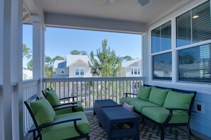 A covered porch with green furniture and a view of neighboring houses.