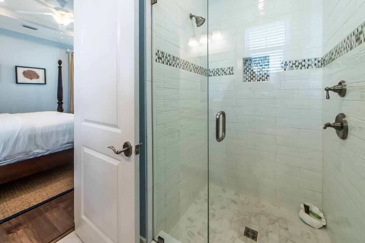 A bedroom with a bed, a bathroom with a glass-enclosed shower, and a door leading to another room.