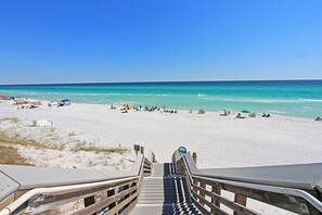 A beach with a wooden staircase leading down to the sand, a clear blue sky, and the ocean in the background.
