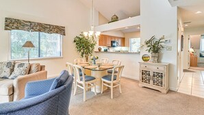 Een moderne woonkamer met een eetgedeelte, met een tafel met glazen blad, witte stoelen en een kroonluchter.