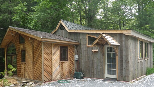 Eine Holzhütte mit Satteldach, einer Haustür und zwei Fenstern.