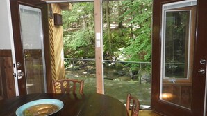 Ein Essbereich mit Tisch und Stühlen, einer Schüssel mit Essen und Blick auf einen Wald durch offene Türen.