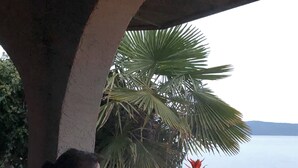A person sitting on a bench under a structure with a view of a body of water and palm trees. - Beachfront Cozy Duplex, Hot Tub BBQ  Adult Only clam/oyster kayak rental (Qualicum Beach)