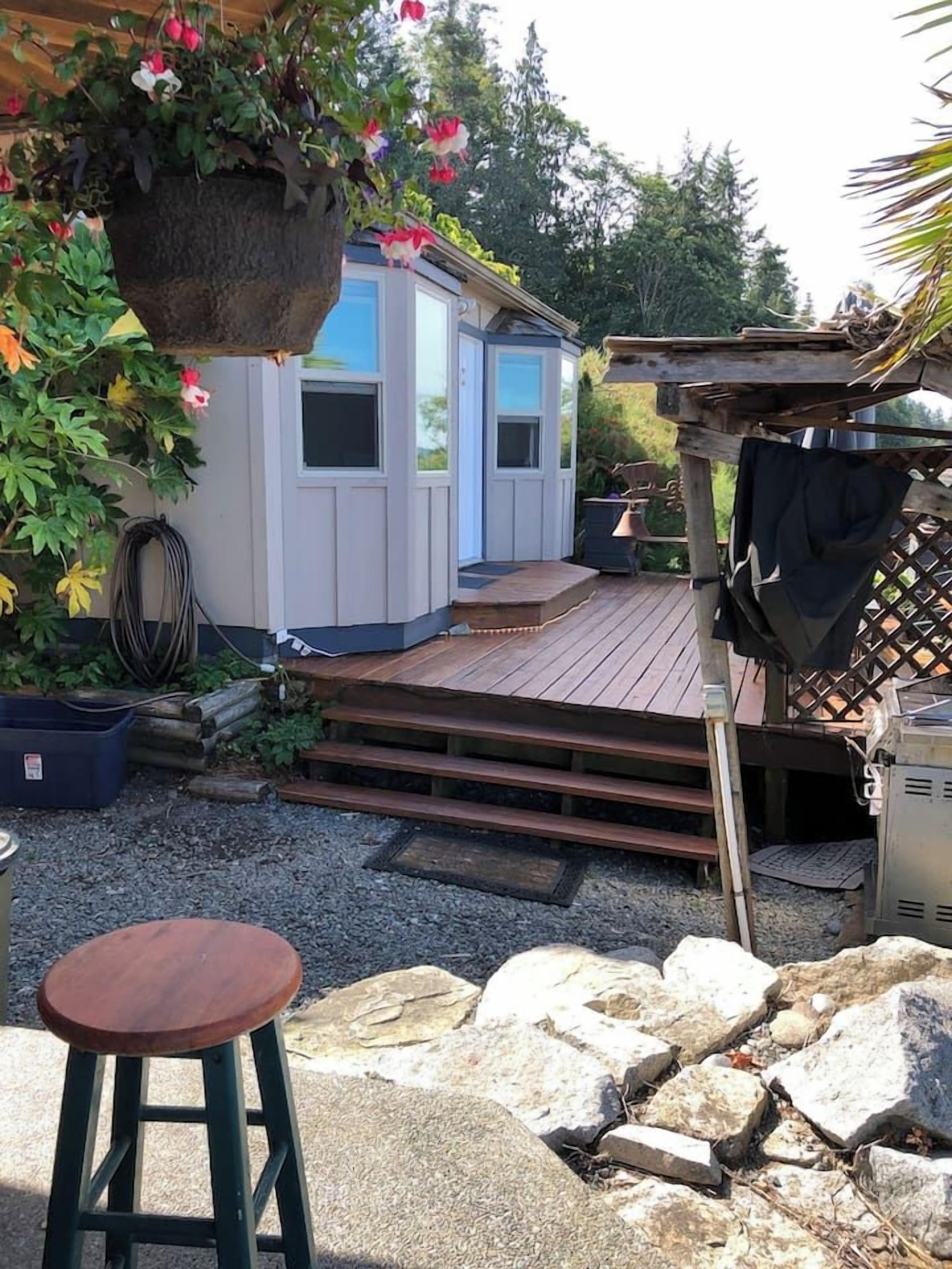 Un cobertizo pequeño con una terraza de madera, una maceta colgante y una parrilla.