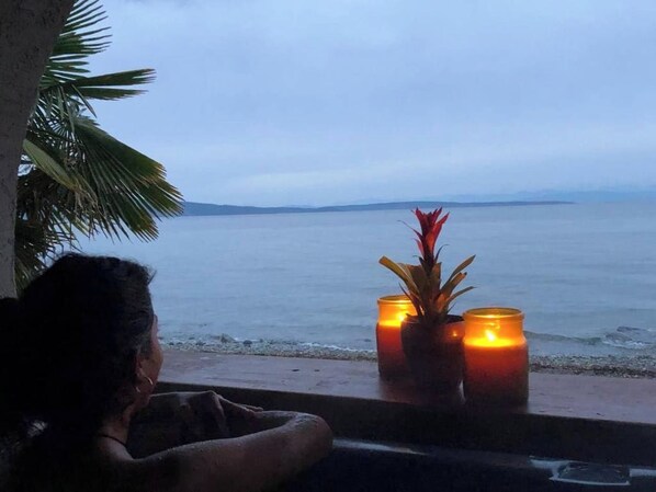 A person seated by a window overlooking a beach with two lit candles on a windowsill.