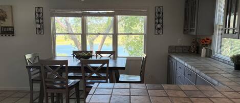 A kitchen with a dining table, chairs, a ceiling fan, and a window with a view of trees.
