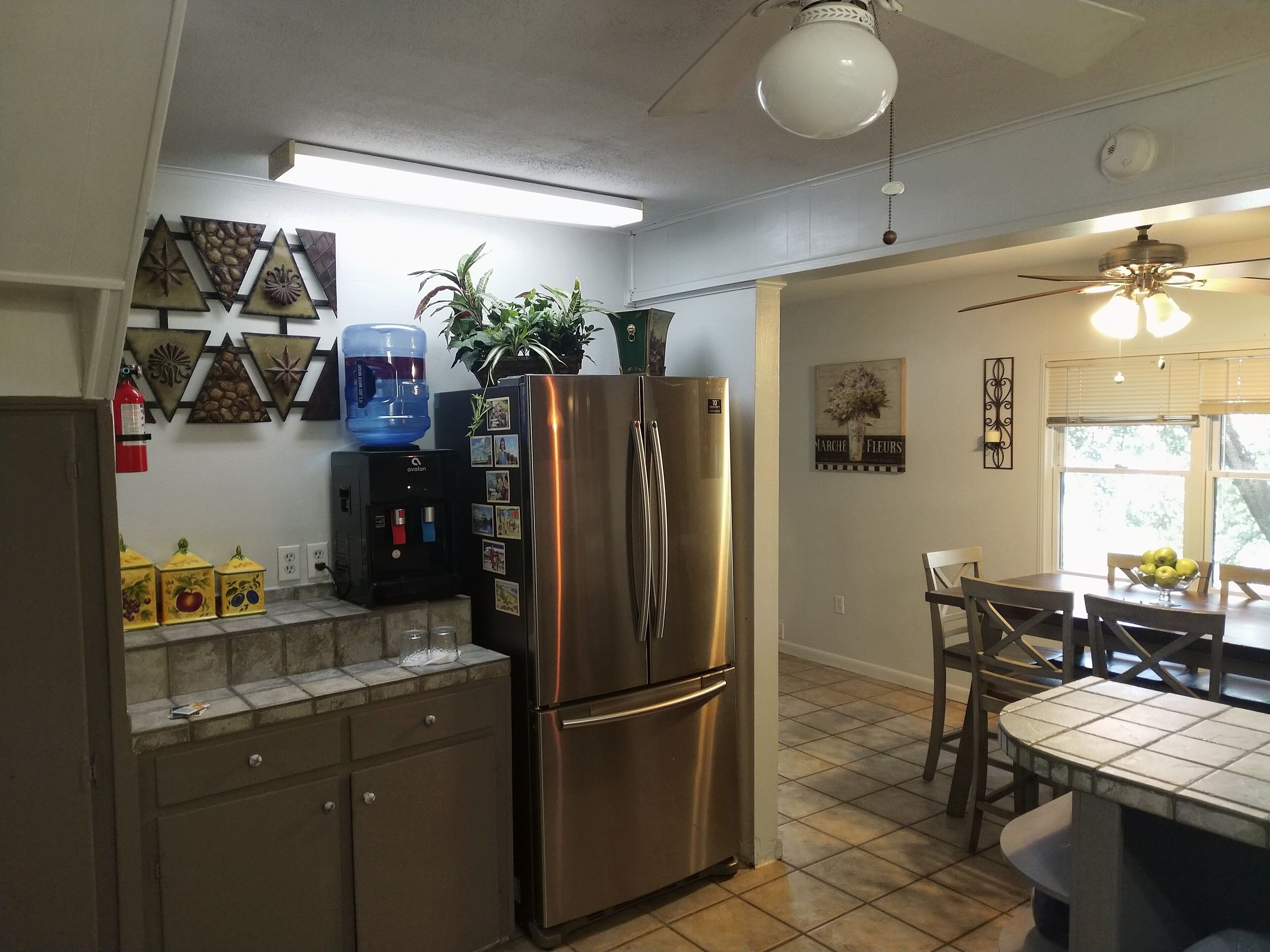A kitchen with a stainless steel refrigerator, a water dispenser, and a dining area with a table and chairs.