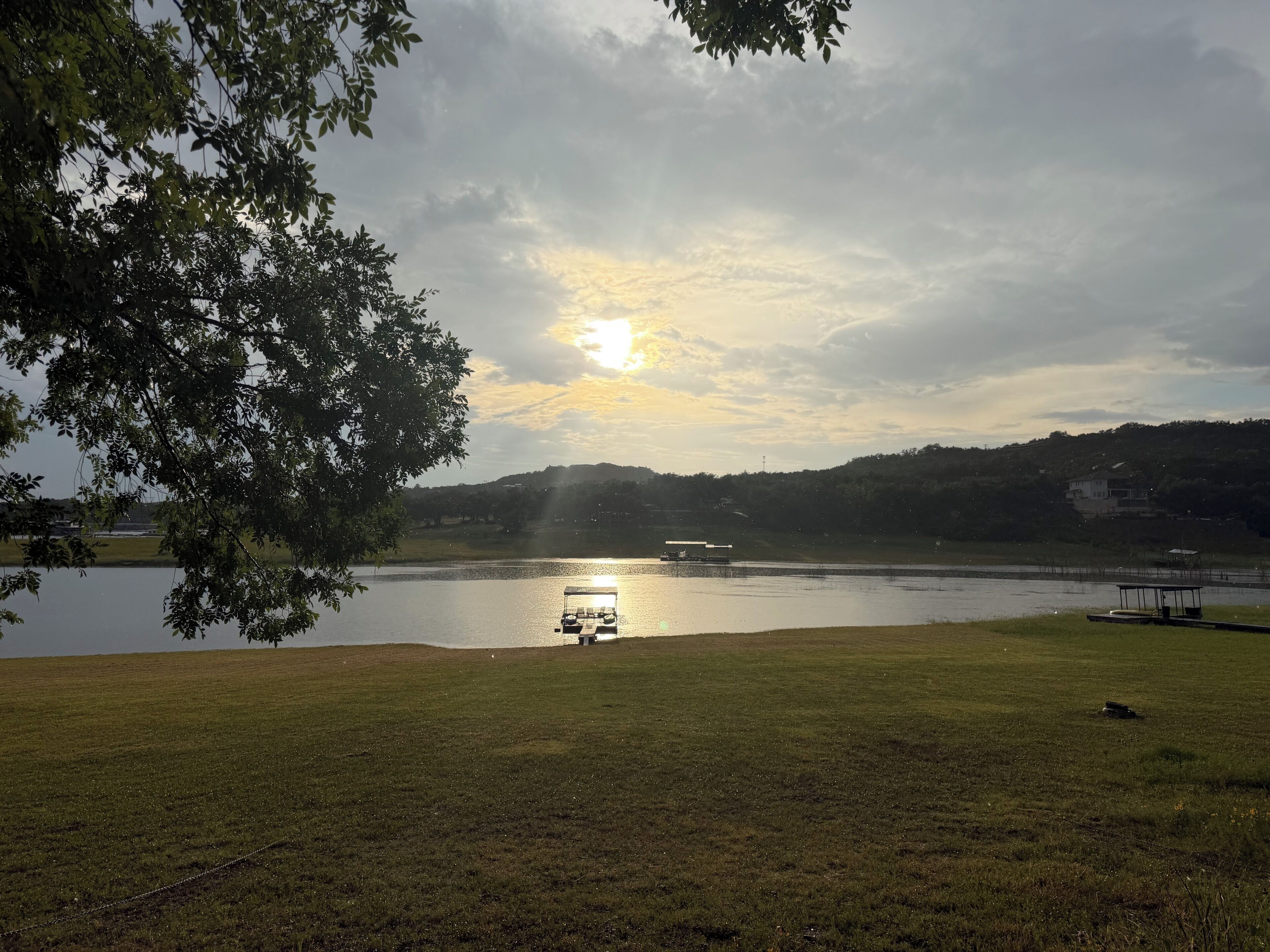 A lake with a boat dock, grassy banks, and a tree in the foreground.
