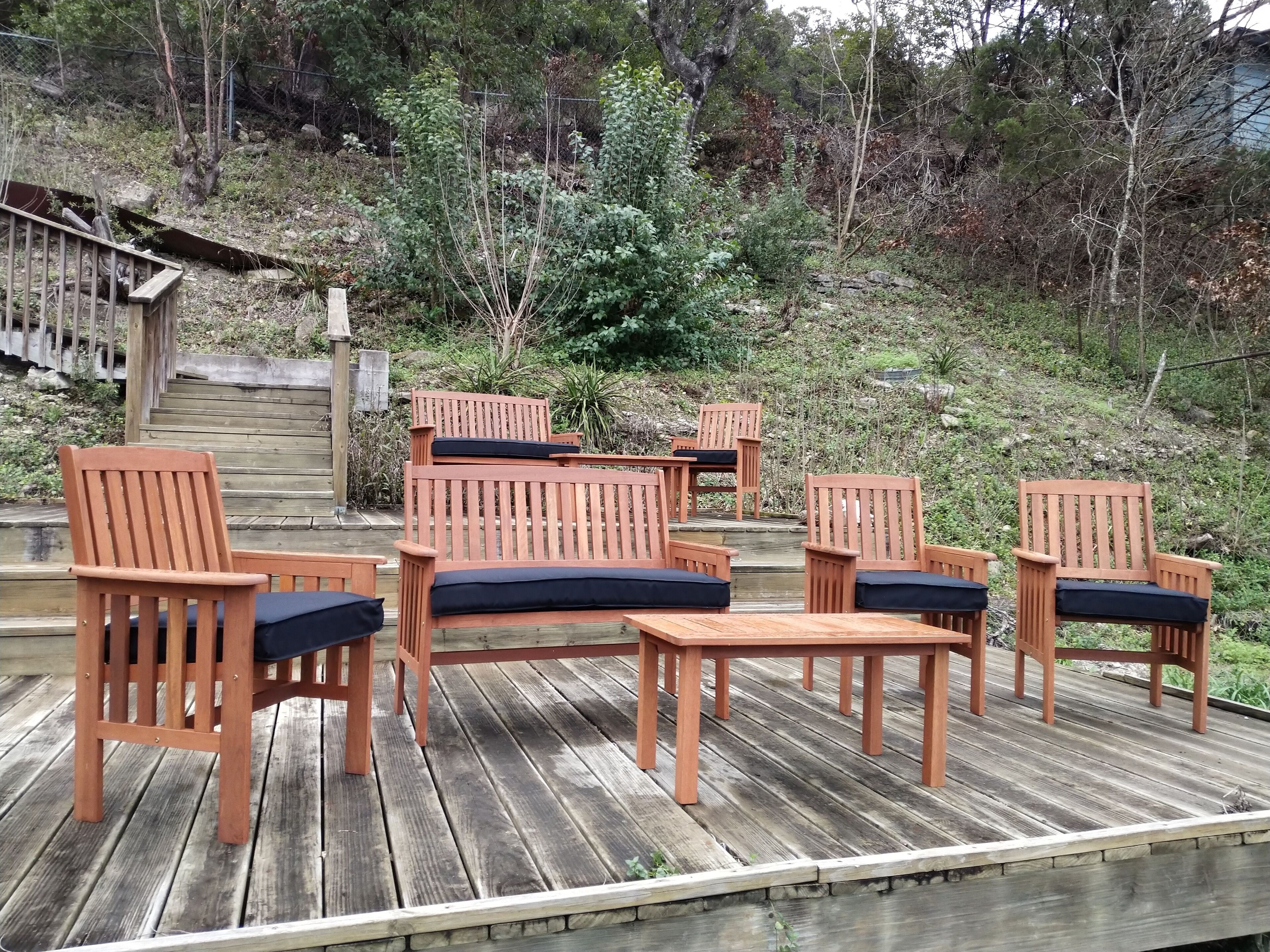 A wooden deck with outdoor furniture, including chairs and a table, overlooking a forested area.