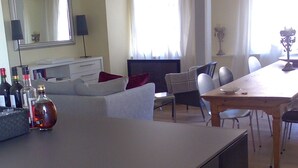Ein modernes Wohnzimmer mit Flachbildfernseher, einer Couch, einem Esstisch mit Stühlen und einer kleinen K üchenzeile inklusive Kühlschrank.
