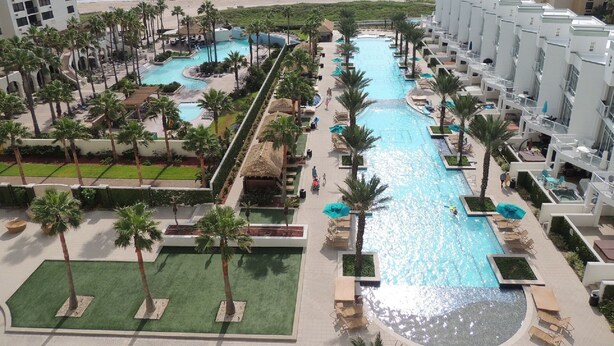 Un resort con varias piscinas, palmeras y vista a la playa.