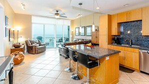 Una cocina moderna con una isla central, taburetes de bar, armarios de madera y un ventanal con vistas a un balcón.