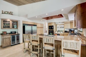 A modern kitchen with wooden cabinets, a stainless steel refrigerator, and a central island with bar stools. - A river runs through. Private Estate on OAK CREEK! Pickleball Court in backyard! (Sedona)