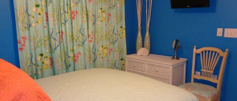 A bedroom with a bed, a dresser, a chair, a television on the wall, and a curtain with a floral pattern.