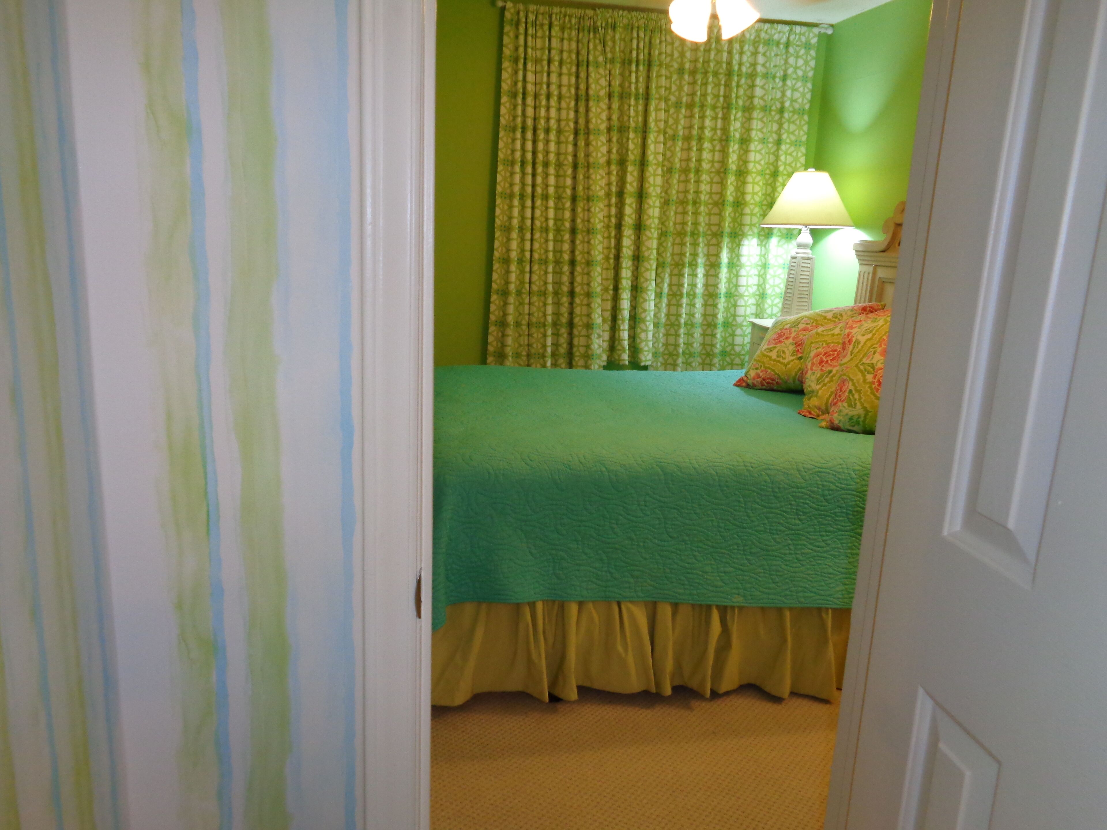 Een slaapkamer met een groene sprei, gele gordijnen en een kussen met een patroon.