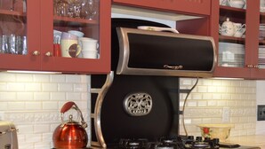 Una cocina vintage con estufa negra, armarios rojos y una tetera sobre la encimera.