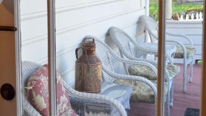Vista a través de una ventana con sillas de mimbre y un recipiente metálico antiguo.