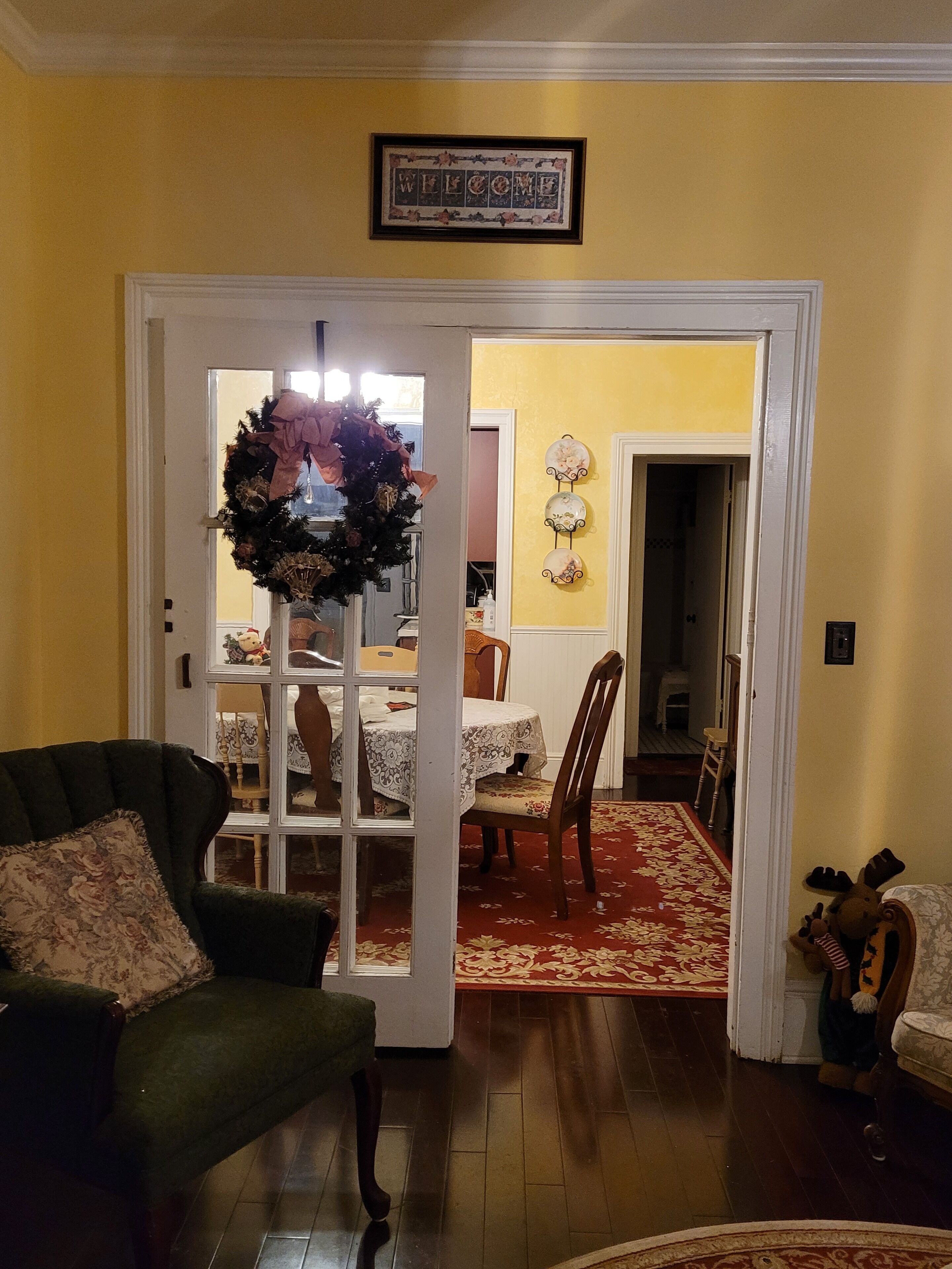 Un salon avec un fauteuil vert, un coin repas avec une table et des chaises, et un couloir menant à une autre pièce.