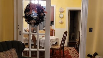 Un salon avec un fauteuil vert, un coin repas avec une table et des chaises, et un couloir menant à une autre pièce.