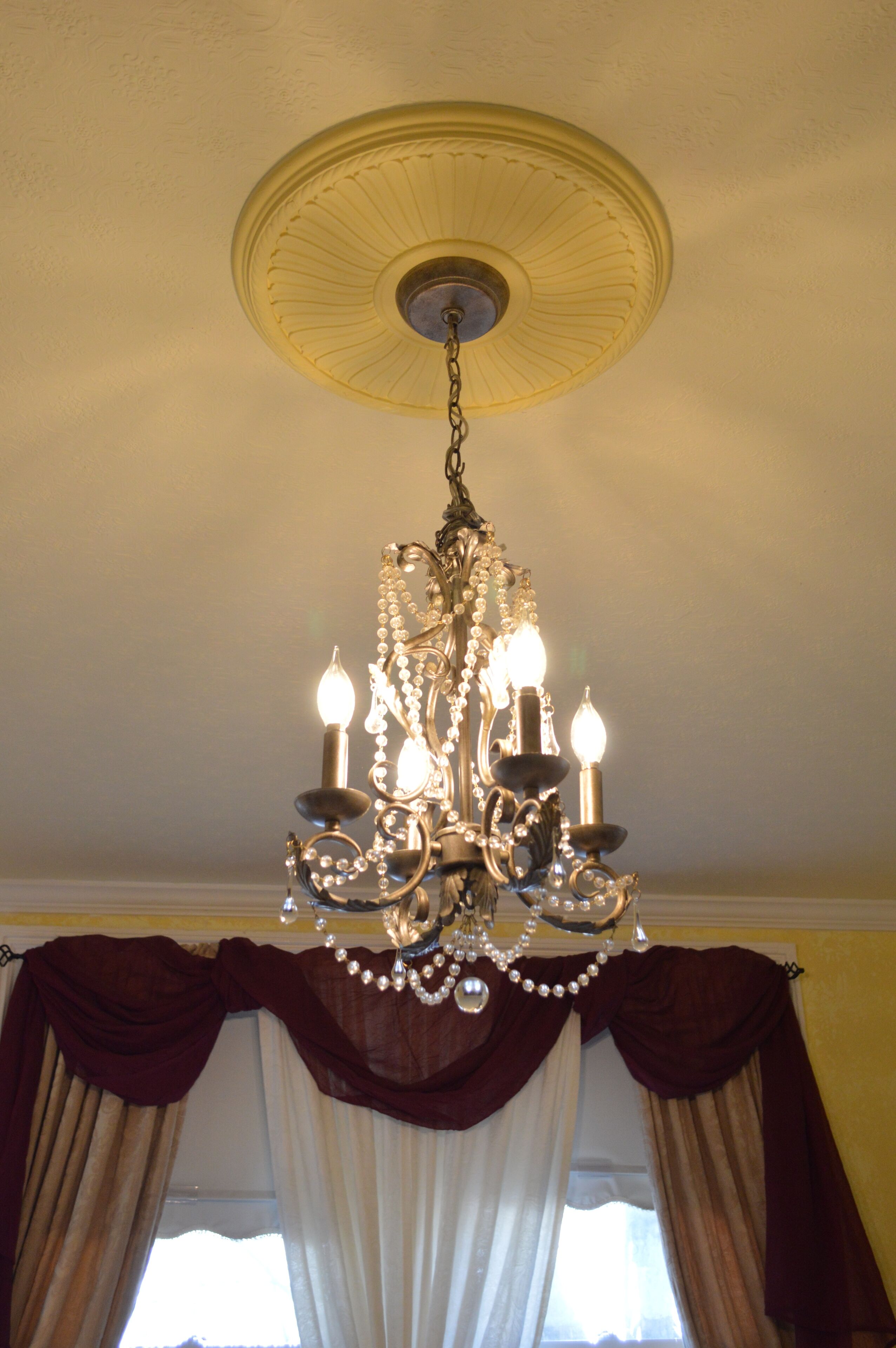A chandelier with multiple candle-like lights, a decorative ceiling medallion, and draped curtains.