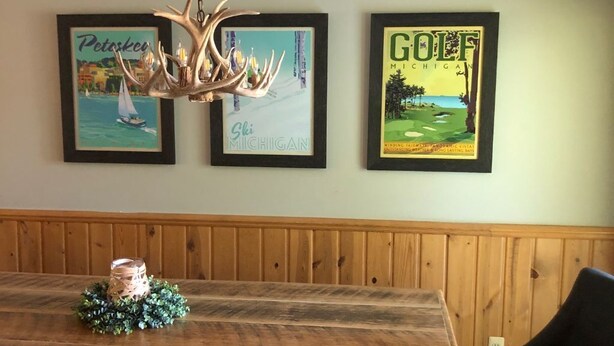Une table à manger en bois, avec des bancs, un lustre et deux tableaux encadrés accrochés au mur.
