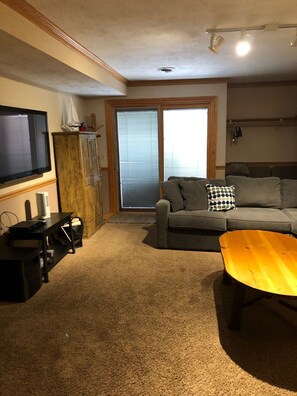 A living room with a grey sofa, a wooden coffee table, a TV on a stand, and a sliding glass door. - Harbor Springs Condo, 2400 Sq. Ft., 5 Bedroom, 3 Bath, 3 Levels, Very Clean (Harbor Springs)