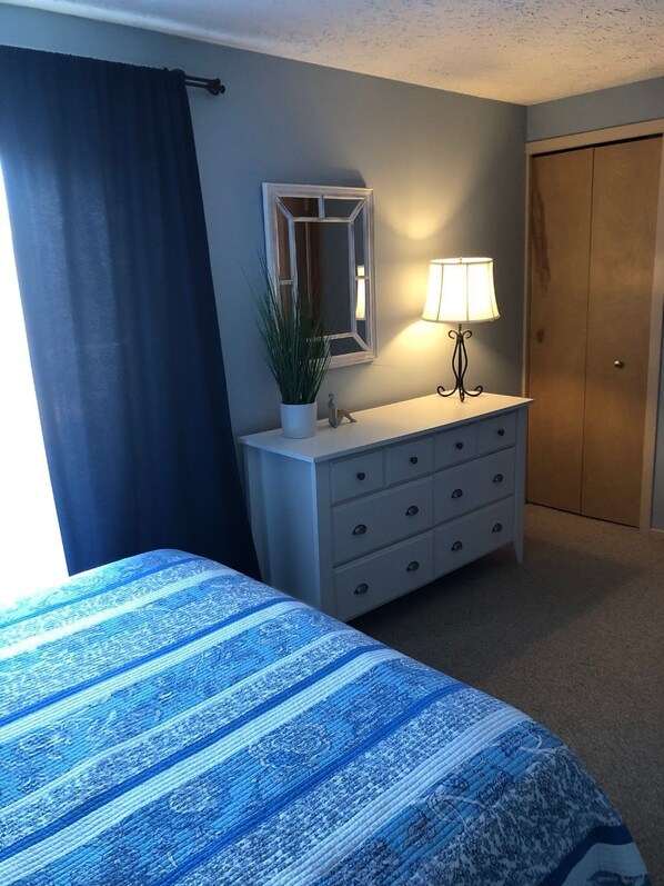 A bedroom with a bed, a dresser, a mirror, a lamp, and a door.