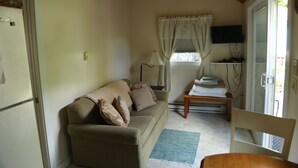 Een knusse woonkamer met een bank, een bijzettafeltje, een aan de muur bevestigde televisie en een raam met gordijnen.