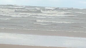 Een strand met golven die op het strand breken onder een bewolkte lucht.