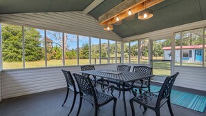 Un patio cubierto con una mesa, sillas, ventanas amplias y vistas al exterior.