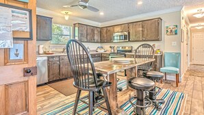 Una cocina con armarios de madera, una mesa de comedor con sillas, un ventilador de techo y un microondas.