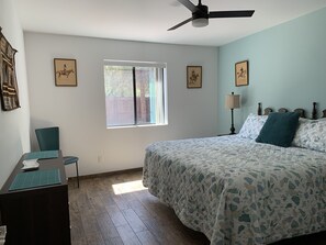 Ein Schlafzimmer mit Bett, Schreibtisch, Stuhl, Fenster und Deckenventilator.
