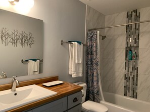 Ein modernes Badezimmer mit einem Holzkosmetikschrank, einem weißen Waschbecken, einer Toilette und einer Dusche mit einem gemusterten Vorhang.
