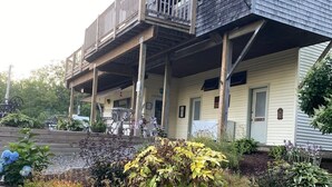 A two-story building with a balcony, wooden deck, and a garden area with various plants. - Ocean View Apartment Along Maine's Scenic Penobscot Bay (Belfast)