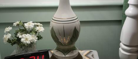 A bedside table with a lamp, a digital clock displaying 8:24, and a vase with white flowers.