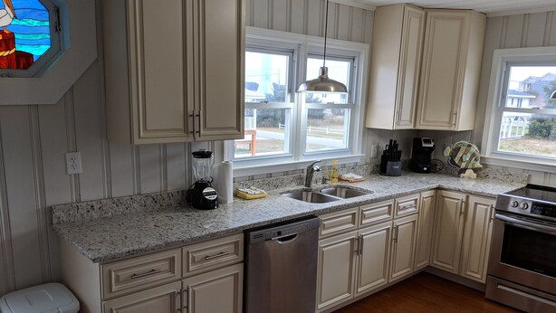 A kitchen with white cabinets, a granite countertop, a dishwasher, a stove, and a window with a view of the outside. - Ocean view, Pet Friendly house with private swimming pool! Sleeps 10. (North Myrtle Beach)