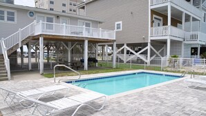A swimming pool with lounge chairs, a covered deck, and a fenced area with a grill. - Ocean view, Pet Friendly house with private swimming pool! Sleeps 10. (North Myrtle Beach)