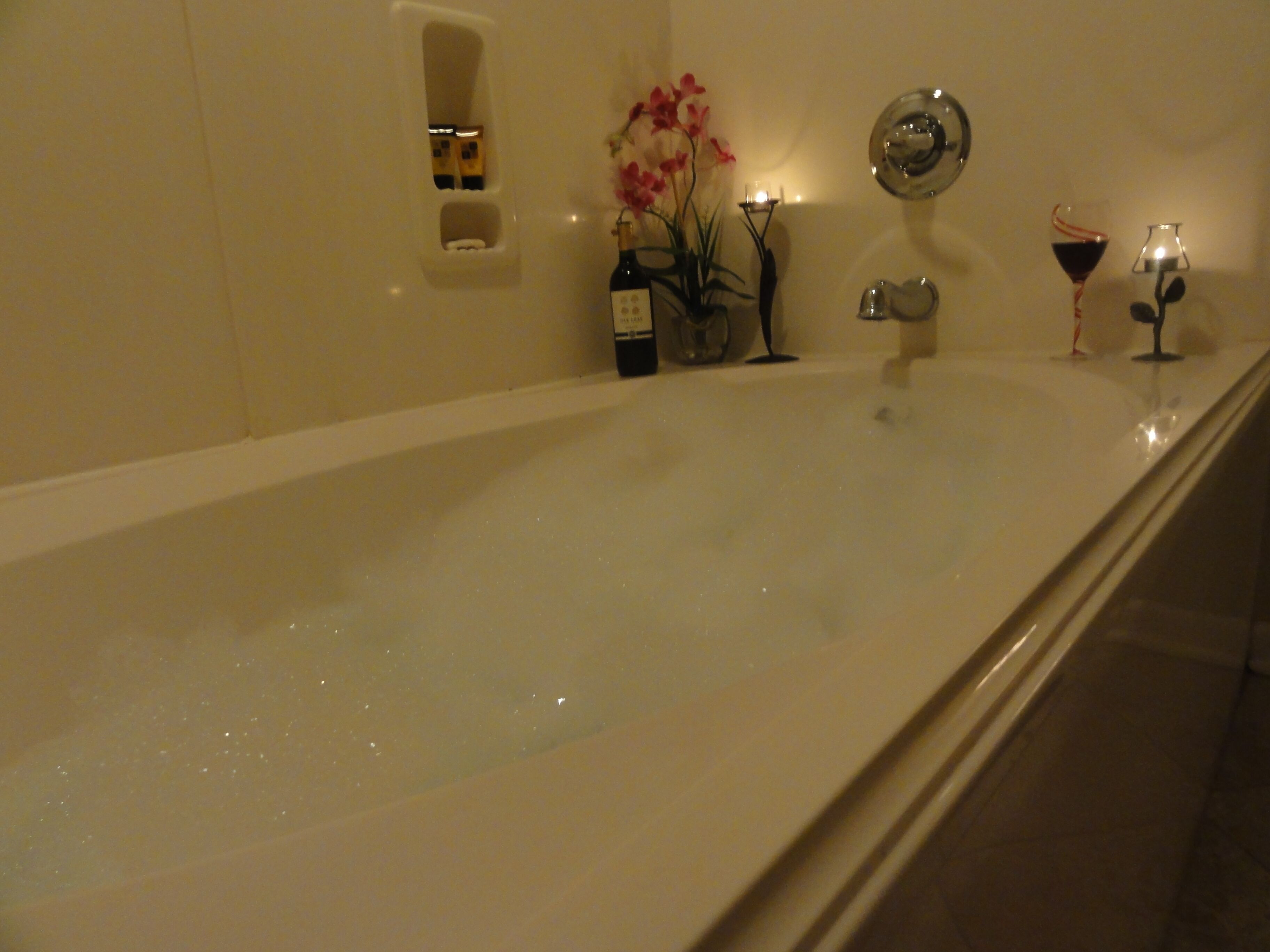 Una bañera grande con una copa de vino tinto y una botella de perfume a un lado.