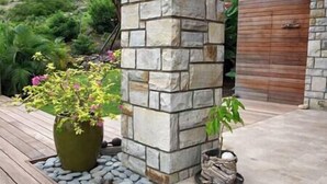 Un pilar de piedra con una planta en maceta y una pequeña olla sobre una terraza de madera.