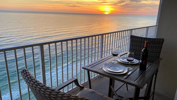Un balcone con un tavolo apparecchiato per due, con vista sull'oceano al tramonto.