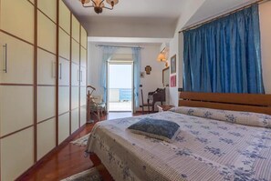 Relax in this serene bedroom with a large bed, wooden wardrobe, and piano, offering a view of the sea.
