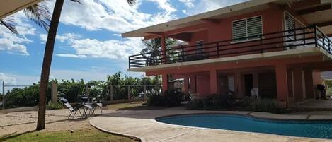 A two-story building with a swimming pool, outdoor seating, and a covered area.